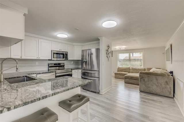 kitchen with white cabinets, a kitchen breakfast bar, light stone counters, kitchen peninsula, and stainless steel appliances