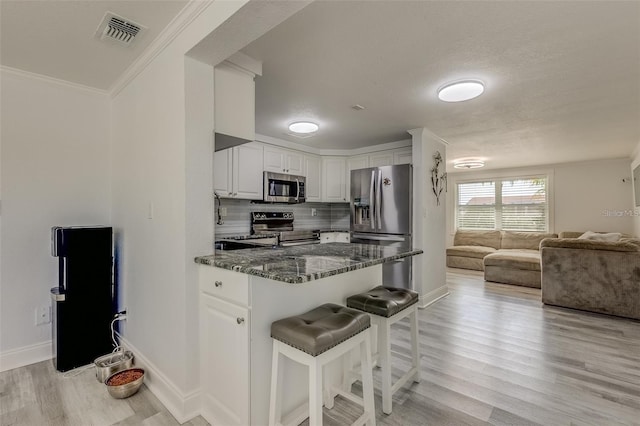 kitchen featuring crown molding, dark stone countertops, appliances with stainless steel finishes, a kitchen bar, and white cabinetry