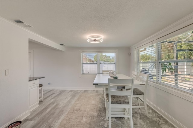 dining space featuring ornamental molding, a textured ceiling, and light hardwood / wood-style flooring