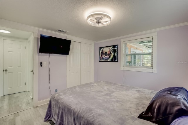 bedroom featuring light hardwood / wood-style floors, ornamental molding, a textured ceiling, and a closet