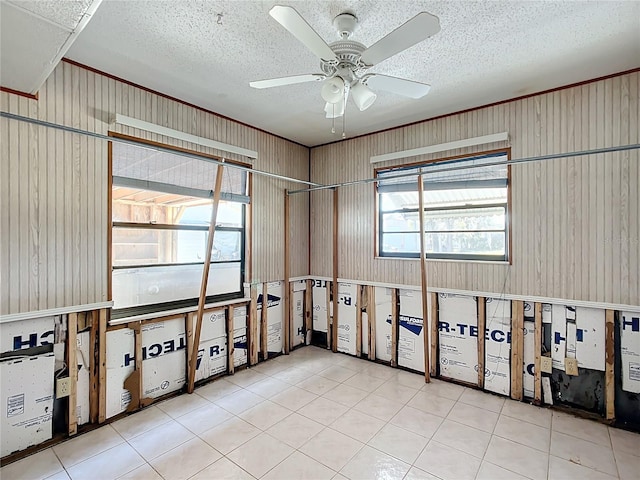 spare room with a textured ceiling, ceiling fan, wooden walls, and light tile patterned flooring