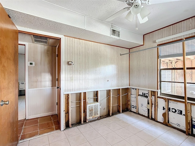 empty room featuring ceiling fan, wood walls, and light tile patterned floors