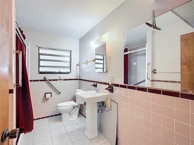 bathroom featuring a textured ceiling, tile patterned flooring, tile walls, and toilet