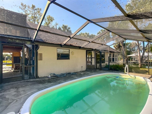 view of pool featuring glass enclosure, a patio area, and a water view