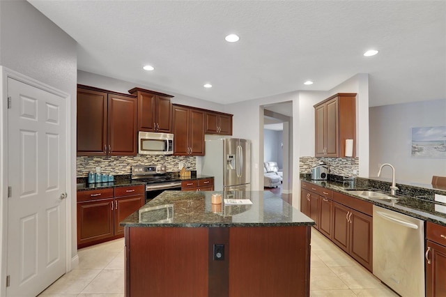 kitchen featuring light tile patterned floors, stainless steel appliances, dark stone countertops, a kitchen island, and sink