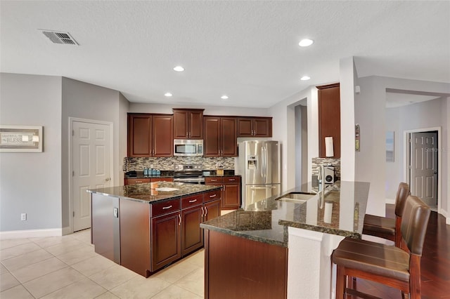 kitchen featuring appliances with stainless steel finishes, dark stone countertops, sink, light tile patterned flooring, and a breakfast bar area