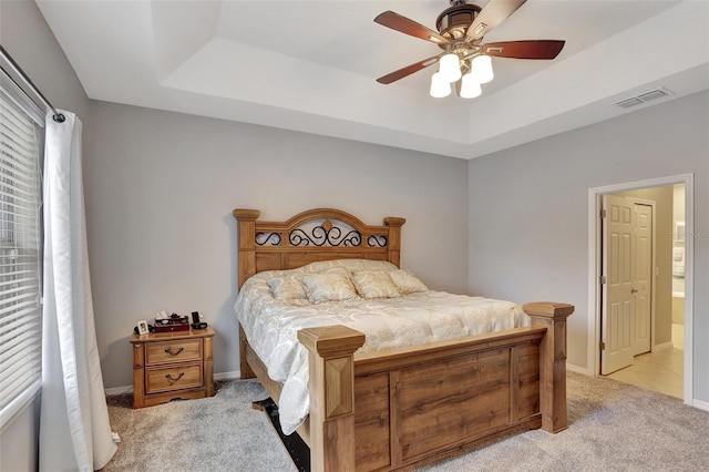 bedroom featuring ceiling fan, ensuite bath, light carpet, and a tray ceiling