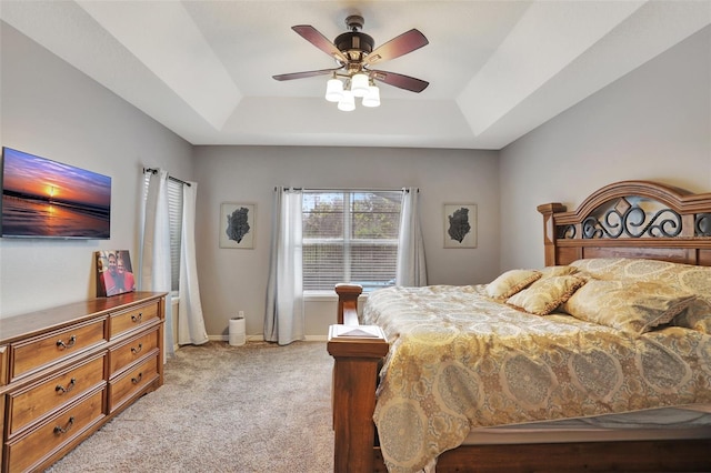 carpeted bedroom with a raised ceiling and ceiling fan