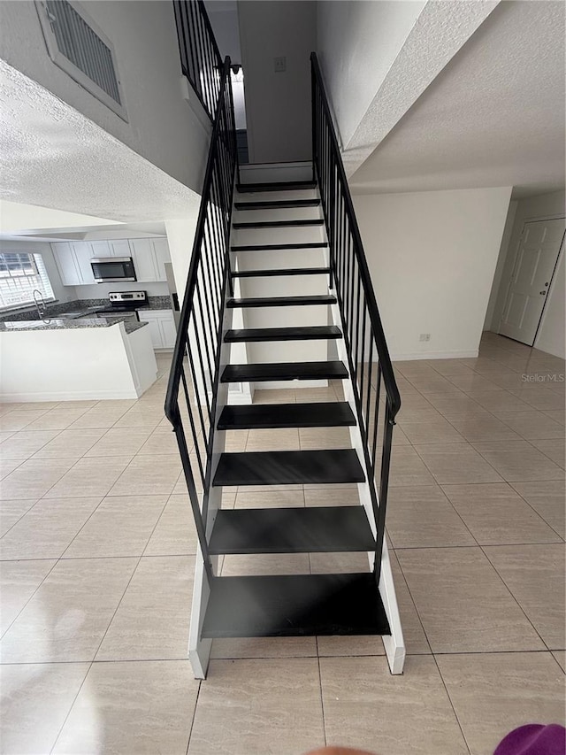 staircase with tile patterned flooring, sink, and a textured ceiling