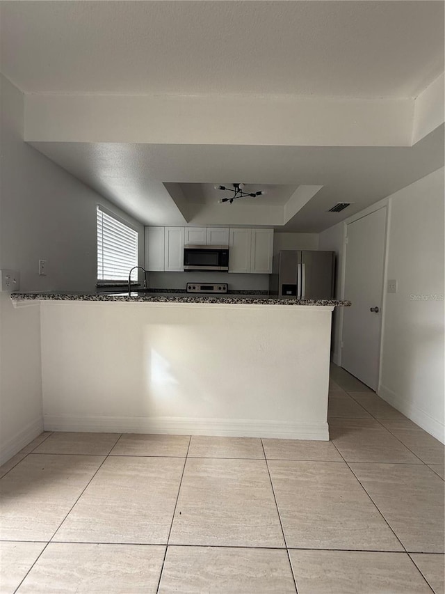 kitchen featuring a tray ceiling, white cabinets, dark stone counters, kitchen peninsula, and stainless steel appliances