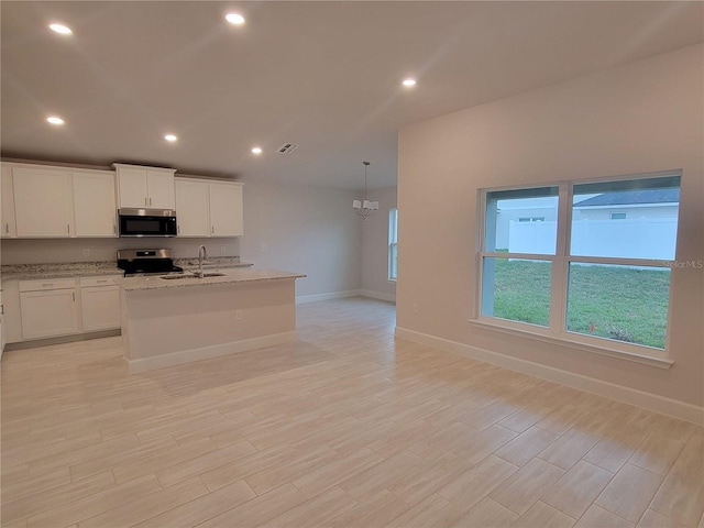 kitchen with light stone counters, decorative light fixtures, stainless steel appliances, an island with sink, and white cabinets