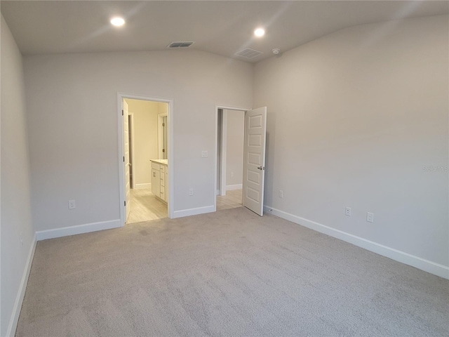 unfurnished bedroom with vaulted ceiling, light colored carpet, and ensuite bath