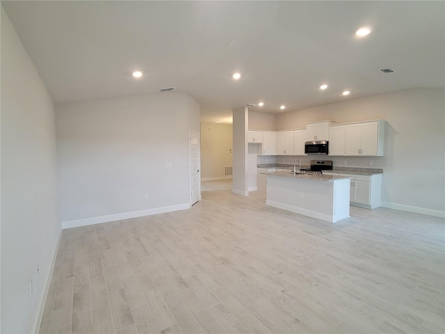 kitchen featuring white cabinets, light hardwood / wood-style floors, light stone countertops, a center island with sink, and appliances with stainless steel finishes