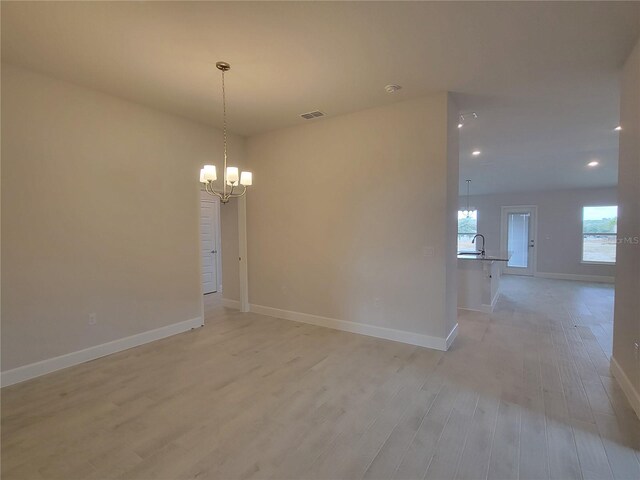 unfurnished room with light wood-type flooring, baseboards, a sink, visible vents, and a notable chandelier