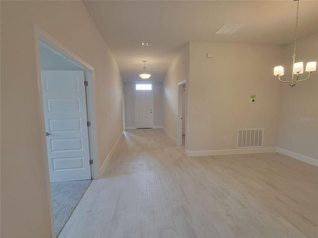 corridor with light wood finished floors, baseboards, visible vents, and a chandelier
