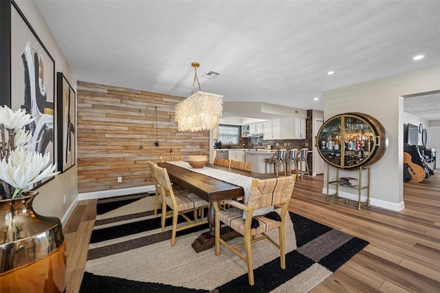 dining area with light hardwood / wood-style floors, a textured ceiling, a notable chandelier, and wooden walls