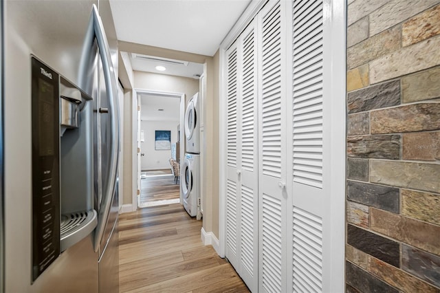 corridor with light wood-type flooring and stacked washer / drying machine