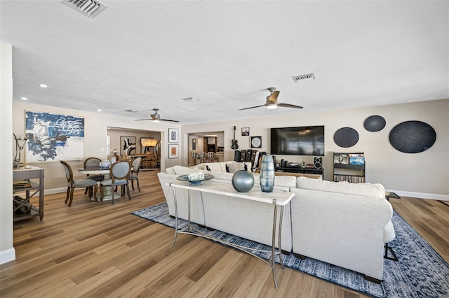 living room featuring light wood-type flooring, ceiling fan, and a textured ceiling