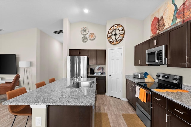 kitchen with stainless steel appliances, an island with sink, a kitchen bar, sink, and light hardwood / wood-style flooring