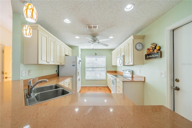 kitchen with cream cabinetry, visible vents, hanging light fixtures, a sink, and white appliances