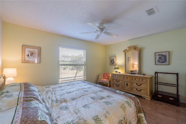 bedroom featuring visible vents, ceiling fan, a textured ceiling, and wood finished floors