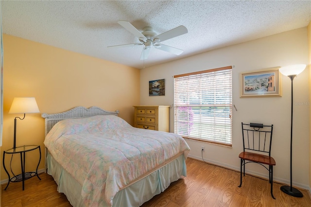 bedroom featuring a textured ceiling, light wood-type flooring, a ceiling fan, and baseboards