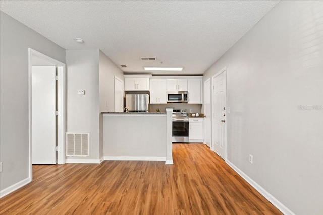 kitchen with stainless steel appliances, a textured ceiling, light wood-type flooring, and white cabinetry