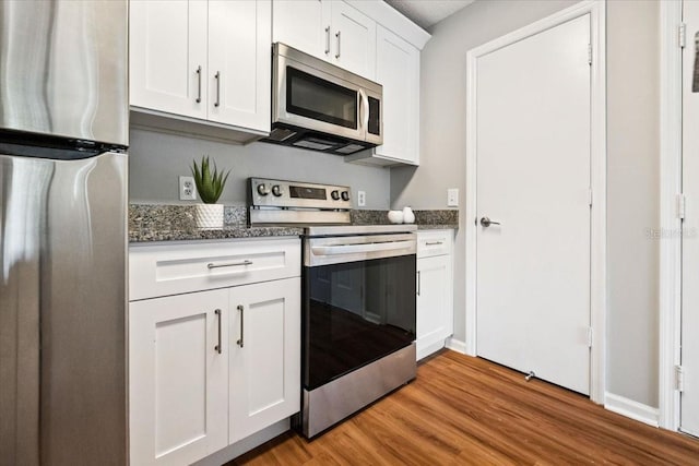 kitchen featuring stainless steel appliances, light hardwood / wood-style floors, dark stone countertops, and white cabinetry