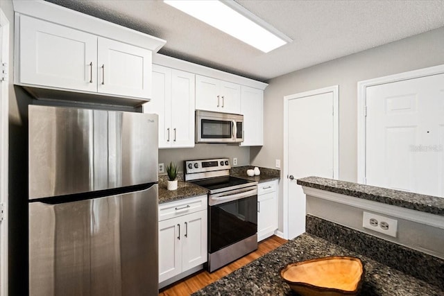 kitchen with stainless steel appliances, white cabinetry, a textured ceiling, light wood-type flooring, and dark stone counters