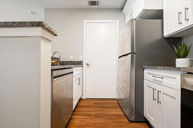 kitchen featuring stainless steel appliances, dark stone counters, wood-type flooring, and white cabinetry