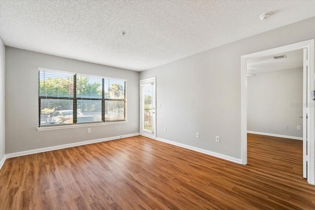 spare room with a textured ceiling, a wealth of natural light, and hardwood / wood-style floors