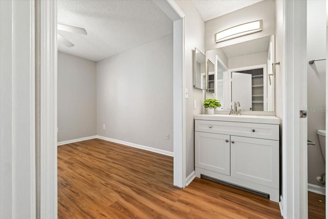 bathroom with toilet, wood-type flooring, vanity, ceiling fan, and a textured ceiling