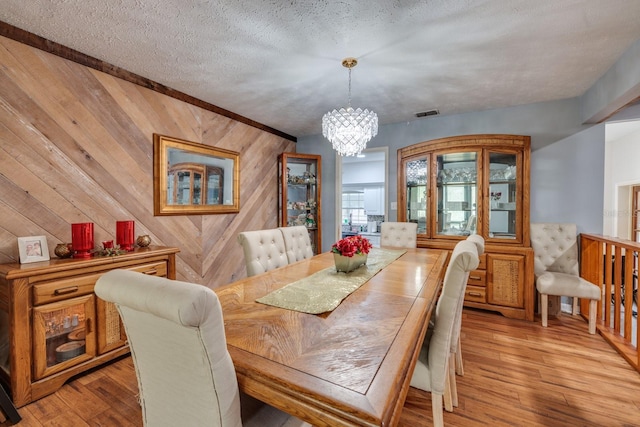 dining room with light hardwood / wood-style floors, a textured ceiling, wood walls, and a notable chandelier