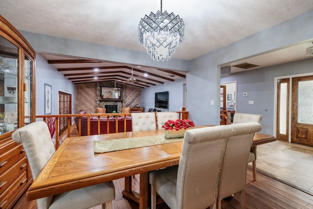 dining space with a fireplace, a textured ceiling, vaulted ceiling with beams, and a notable chandelier