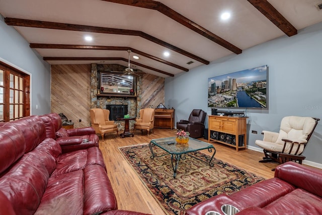 living room with hardwood / wood-style flooring, wooden walls, vaulted ceiling with beams, and a stone fireplace