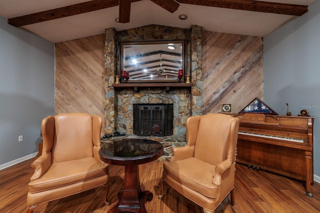 sitting room with lofted ceiling with beams, a stone fireplace, wooden walls, and wood-type flooring