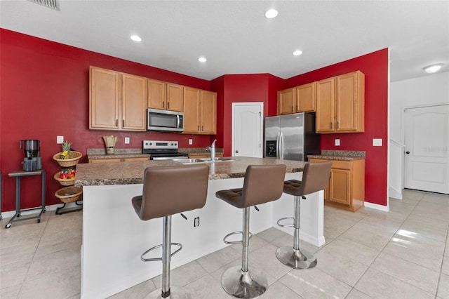 kitchen with light tile patterned flooring, sink, a breakfast bar area, appliances with stainless steel finishes, and a kitchen island with sink