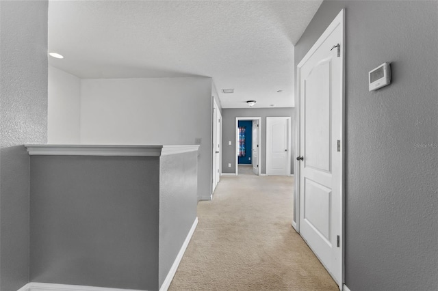 hallway with light carpet and a textured ceiling