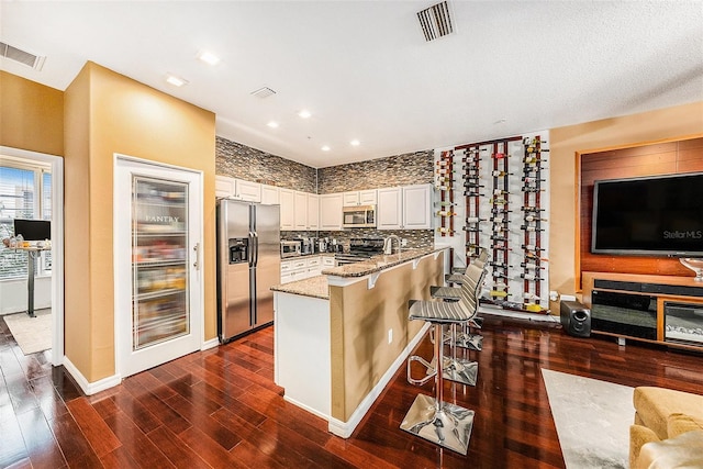 kitchen featuring kitchen peninsula, a kitchen bar, light stone countertops, stainless steel appliances, and white cabinets