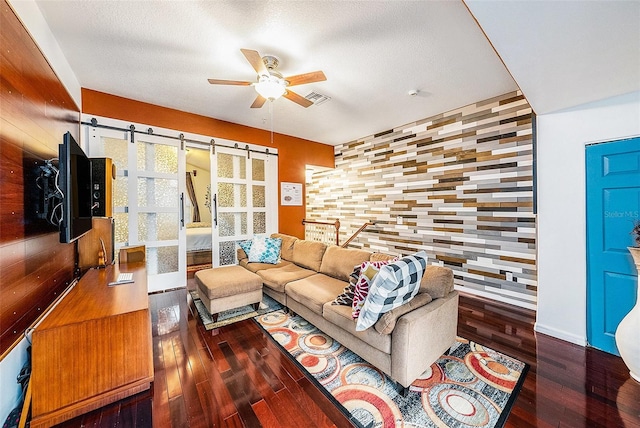 living room with dark wood-type flooring, a barn door, and ceiling fan