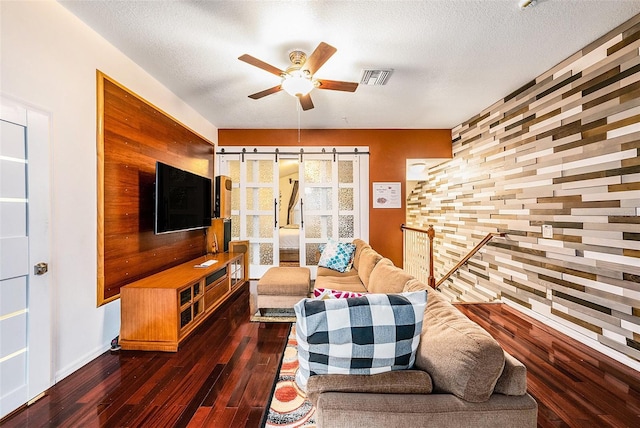 living room featuring a textured ceiling, dark wood-type flooring, a barn door, and ceiling fan