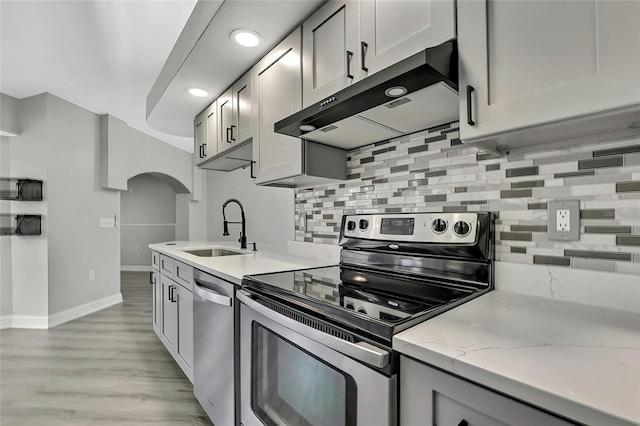 kitchen featuring light stone countertops, sink, stainless steel appliances, backsplash, and extractor fan