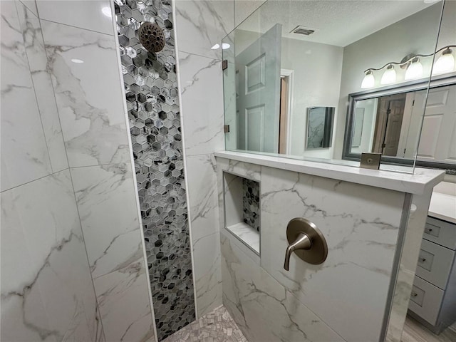 bathroom with a tile shower, vanity, and a textured ceiling