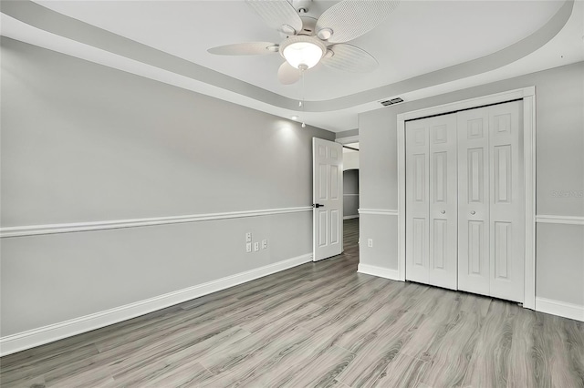 unfurnished bedroom featuring light wood-type flooring, a closet, a tray ceiling, and ceiling fan