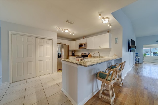 kitchen with light stone countertops, white cabinets, stainless steel appliances, kitchen peninsula, and a breakfast bar