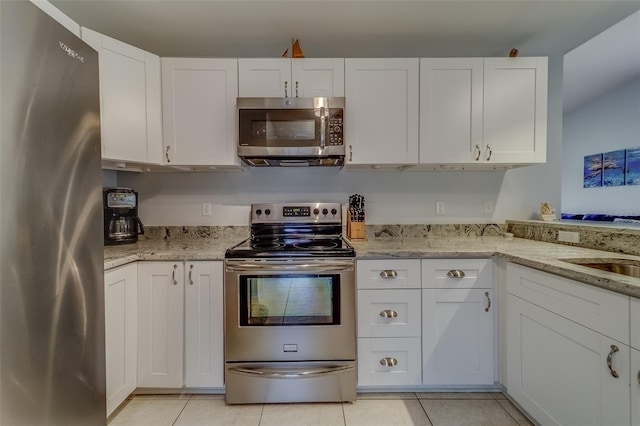 kitchen featuring light tile patterned floors, appliances with stainless steel finishes, white cabinetry, and light stone counters