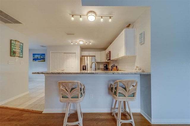 kitchen featuring white cabinets, kitchen peninsula, light stone counters, and stainless steel appliances