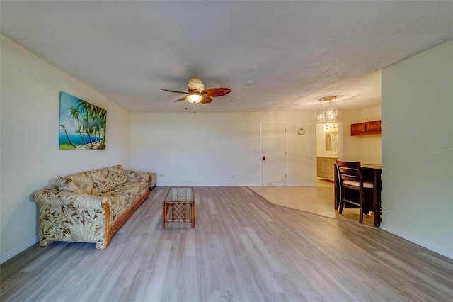 living room featuring ceiling fan with notable chandelier, a textured ceiling, and light wood-type flooring