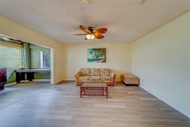 living area with ceiling fan, a textured ceiling, and light wood-type flooring