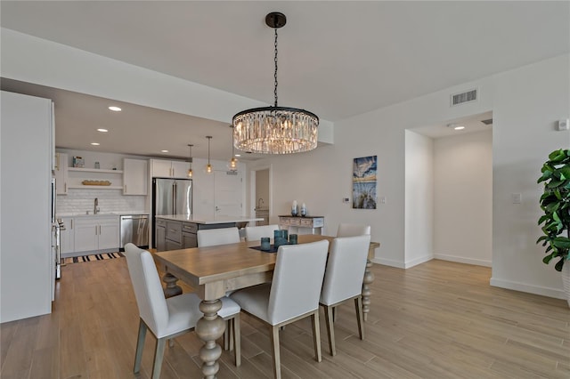 dining space with an inviting chandelier, light hardwood / wood-style flooring, and sink